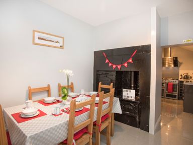 A dining area with a table set for six people and an old black fireplace with a red banner in a home at Hirfron in Llanberis