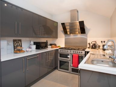 A kitchen with gray cabinets stainless steel stove microwave and sink at Hirfron in Llanberis