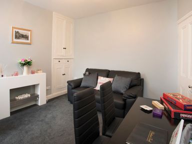 A living room with a black sofa, black dining chairs, a white built-in cabinet, and a white mantel with flowers at Hirfron in Llanberis