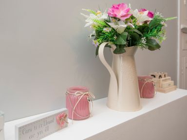 A white pitcher with flowers and pink candle jars on a white shelf at Hirfron in Llanberis