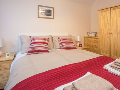 A bedroom with a bed with red and beige bedding wooden furniture and a framed picture on the wall at Hirfron in Llanberis
