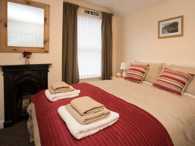A bedroom with a bed with folded towels on a red bedspread a mirror above a fireplace and a window with curtains at Hirfron in Llanberis