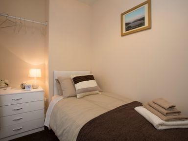 A small bedroom with a single bed a bedside table with a lamp and clock and folded towels on the bed at Hirfron in Llanberis