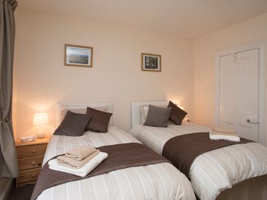 A bedroom with two single beds each with pillows and folded towels on brown runners at Hirfron in Llanberis