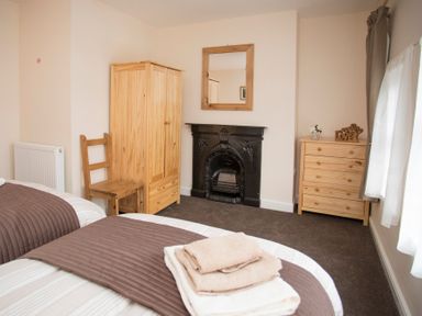 A bedroom with two beds a wooden wardrobe wooden chair chest of drawers and a black fireplace at Hirfron in Llanberis