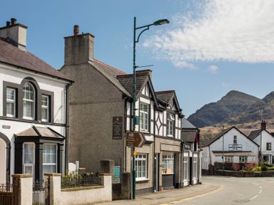 A street view of buildings with a hotel sign and mountains in the background at Hirfron in Llanberis