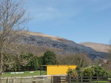 A mountain landscape with trees a yellow structure and fenced grassy area at Hirfron in Llanberis