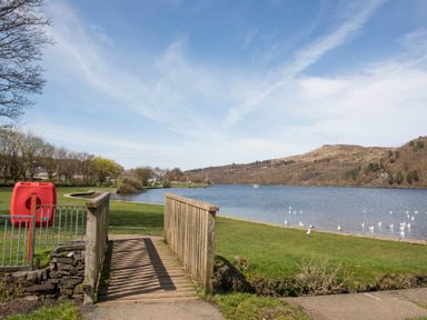 A wooden footbridge over a small stream with a lake and hills in the background at Hirfron in Llanberis