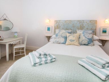 A bedroom with a bed with patterned pillows and folded towels a desk with a lamp and chair and two small framed pictures at Big House in Llandecwyn