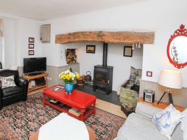 A living room with a wood stove under a wooden beam a red coffee table a television and patterned carpet at Big House in Llandecwyn