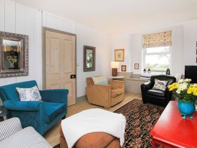 A living room with multiple armchairs a red table with flowers and a window at Big House in Llandecwyn