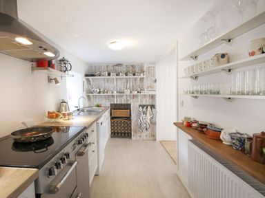 A kitchen with stove sink shelves holding pots dishes and glasses at Big House in Llandecwyn