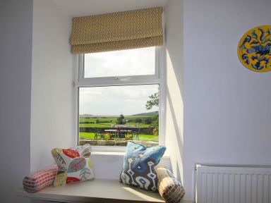 A window with patterned cushions on the sill and a view of outdoor seating area and green fields at Big House in Llandecwyn