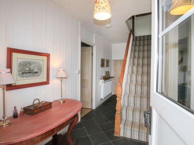 An entry hallway with a striped carpeted staircase a wooden table with two lamps and framed pictures on walls at Big House in Llandecwyn