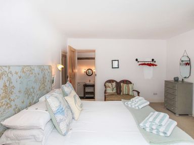 A bedroom with a bed, pillows, a bench, a chest of drawers, mirror, and an open door leading to a bathroom at Big House in Llandecwyn