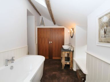 A bathroom with a bathtub sink on a wooden table wooden double doors and a painting on the wall at Big House in Llandecwyn