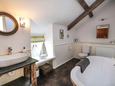 A bathroom with a bathtub a toilet a sink with a mirror a wooden countertop and a window with a model sailboat at Big House in Llandecwyn