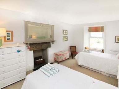 A bedroom with two single beds a white dresser a fireplace and a window at Big House in Llandecwyn