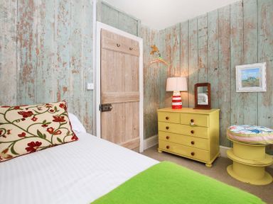 A bedroom with a bed a door a yellow dresser with lamp and mirror and a round stool at Big House in Llandecwyn