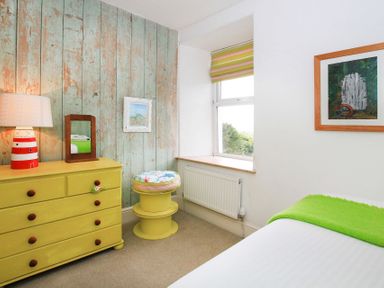 A bedroom with a yellow chest of drawers and stool a window and two framed pictures at Big House in Llandecwyn