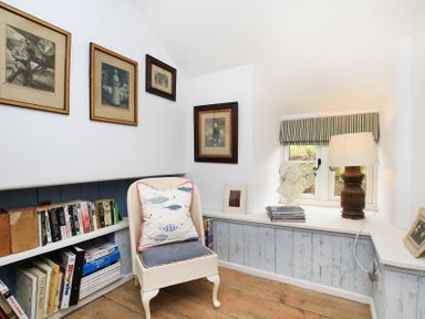 A small reading nook with a chair a pillow books framed pictures a bust a lamp and a window at Big House in Llandecwyn
