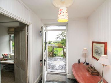 An entryway with an open door leading outside a wooden table with two lamps and a framed picture on the wall at Big House in Llandecwyn