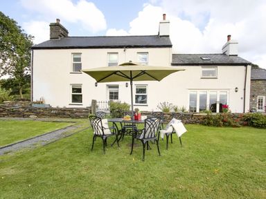 A garden with a metal table and chairs under an umbrella in front of a white house at Big House in Llandecwyn