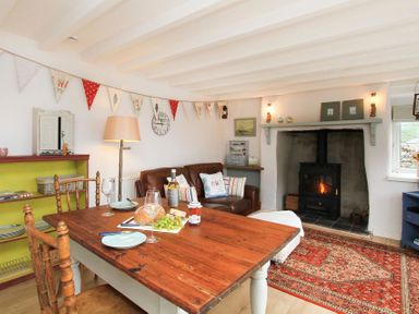 A dining area with wooden table and chairs a leather sofa and a wood burning stove on a rug at Big House in Llandecwyn