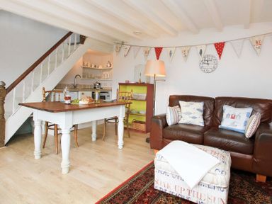 A living room with a brown leather sofa a wooden dining table chairs a staircase and a small kitchen at Big House in Llandecwyn