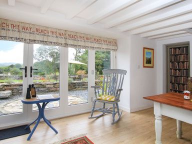 A room with a rocking chair a small table with binoculars and a jar on a wooden table near glass doors at Big House in Llandecwyn