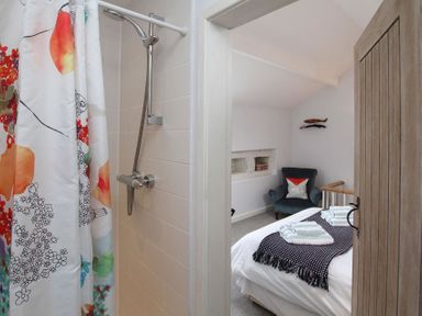 A bathroom shower with a colorful curtain next to a bedroom with a bed towels and a dark armchair at Big House in Llandecwyn