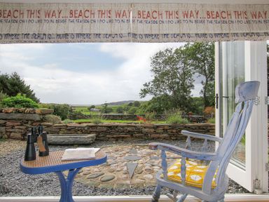 A blue rocking chair with a yellow cushion facing a patio and garden with a stone wall and trees at Big House in Llandecwyn