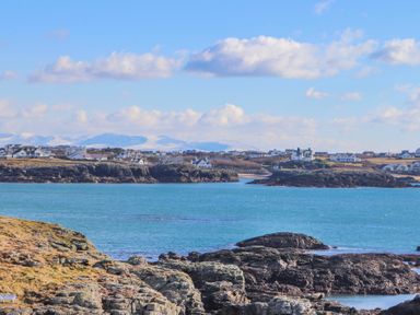 A coastal village with houses along rocky cliffs and blue water at Isallt in Trearddur Bay