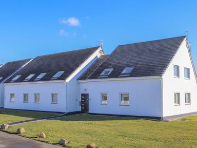 A white two-story residential building with multiple windows and skylights on a green lawn at Isallt in Trearddur Bay
