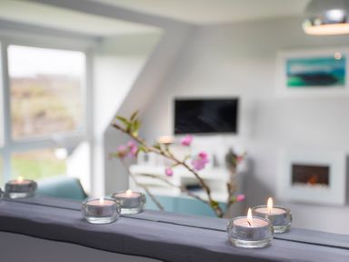 A living room with lit candles on a shelf and a television on the wall at Isallt in Trearddur Bay