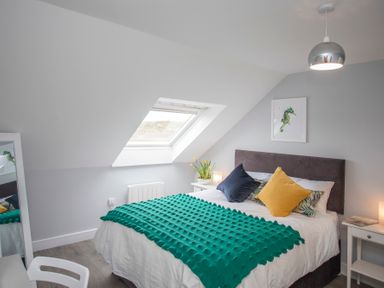 A bedroom with a bed pillows bedside tables and a slanted window at Isallt in Trearddur Bay