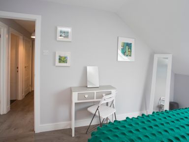A bedroom with a small white desk and mirror white chair and full length mirror by a gray wall at Isallt in Trearddur Bay