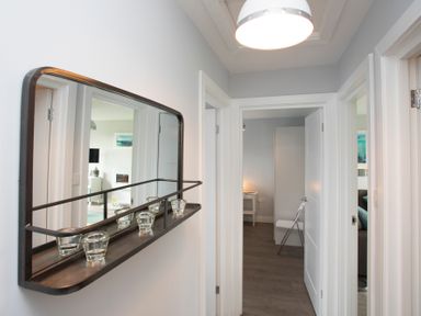 A hallway with a wall mirror holding glass candle holders and doors leading to rooms at Isallt in Trearddur Bay