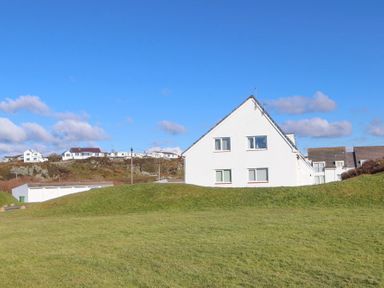 A white house with four windows on a grassy hill under a blue sky at Isallt in Trearddur Bay