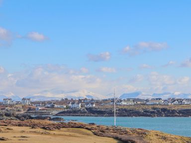 A coastal village with houses near water and snow-covered mountains in the background at Trearddur Bay
