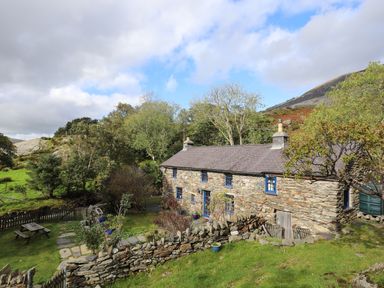 A stone cottage with blue windows and a fenced garden with a picnic table at Llwyn Bedw in Nant Peris