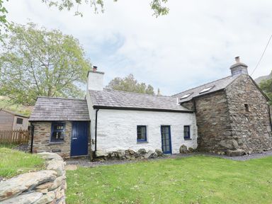 A stone and white cottage with blue doors and windows and a grassy yard at Llwyn Bedw in Nant Peris