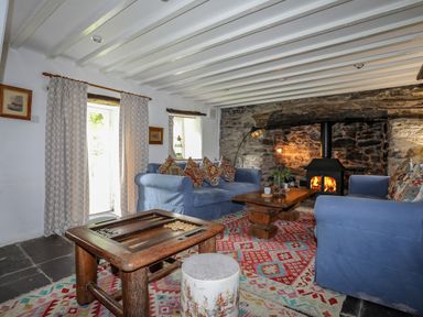 A living room with two blue sofas a wooden coffee table a wood-burning stove and patterned rugs at Llwyn Bedw in Nant Peris