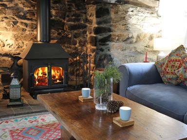 A living room with a wood burning stove a blue sofa with patterned cushions and a wooden coffee table with candles and pine cones at Llwyn Bedw in Nant Peris