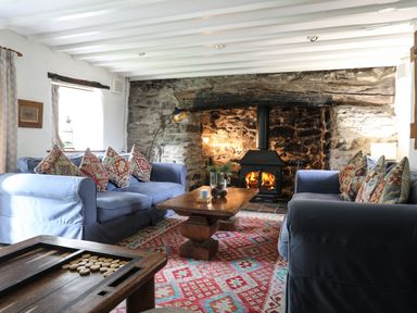A living room with blue sofas patterned cushions a wooden coffee table and a wood burning stove in a stone fireplace at Llwyn Bedw in Nant Peris