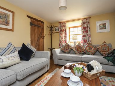 A living room with two gray sofas and patterned cushions by a wooden door at Llwyn Bedw in Nant Peris