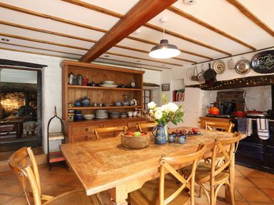 A kitchen with a wooden dining table and chairs a wooden cabinet with dishes and pots and a fireplace with hanging pans at Llwyn Bedw in Nant Peris
