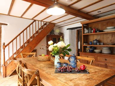 A dining area with a wooden table and chairs next to wooden stairs and a wooden cabinet with dishes at Llwyn Bedw in Nant Peris
