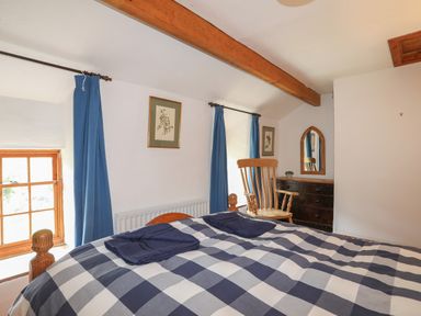 A bedroom with a checkered bedspread blue curtains wooden rocking chair and a dresser with a mirror at Llwyn Bedw in Nant Peris