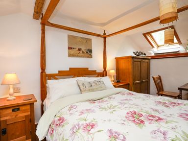A bedroom with a wooden four-poster bed floral bedding wooden nightstands lamps wooden wardrobe and skylight window at Llwyn Bedw in Nant Peris